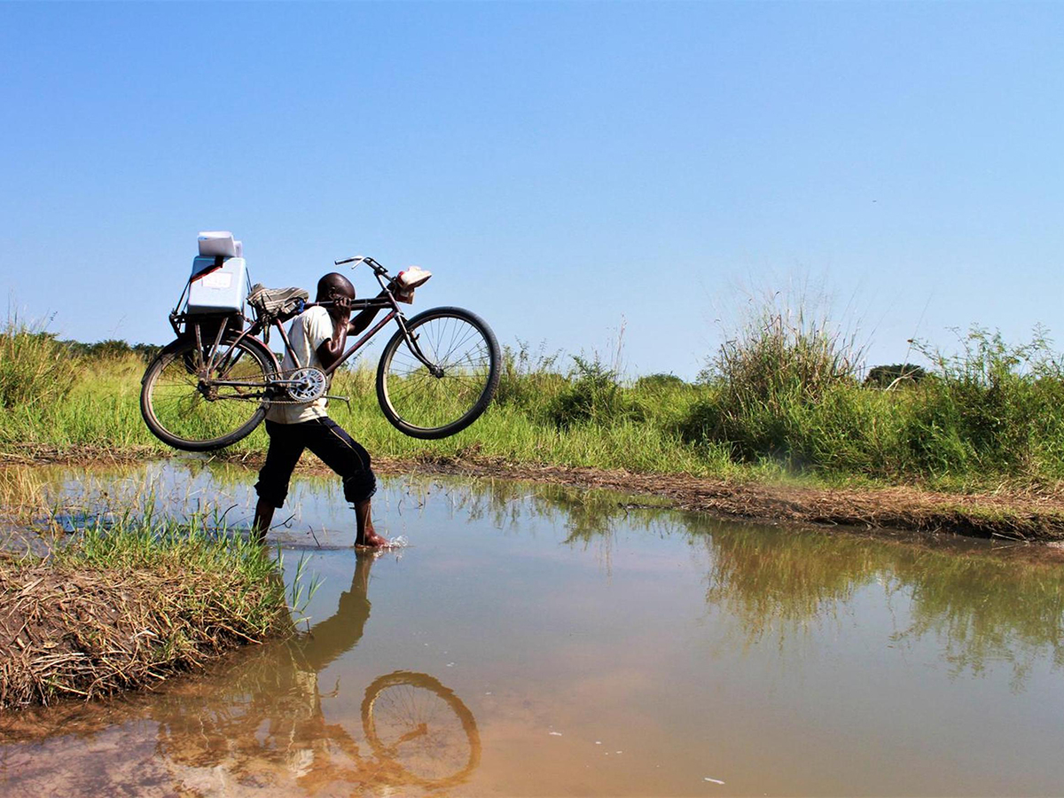 A community relay crosses a water stream with his bike to vaccin - Nők Lapja - Nők Lapja
