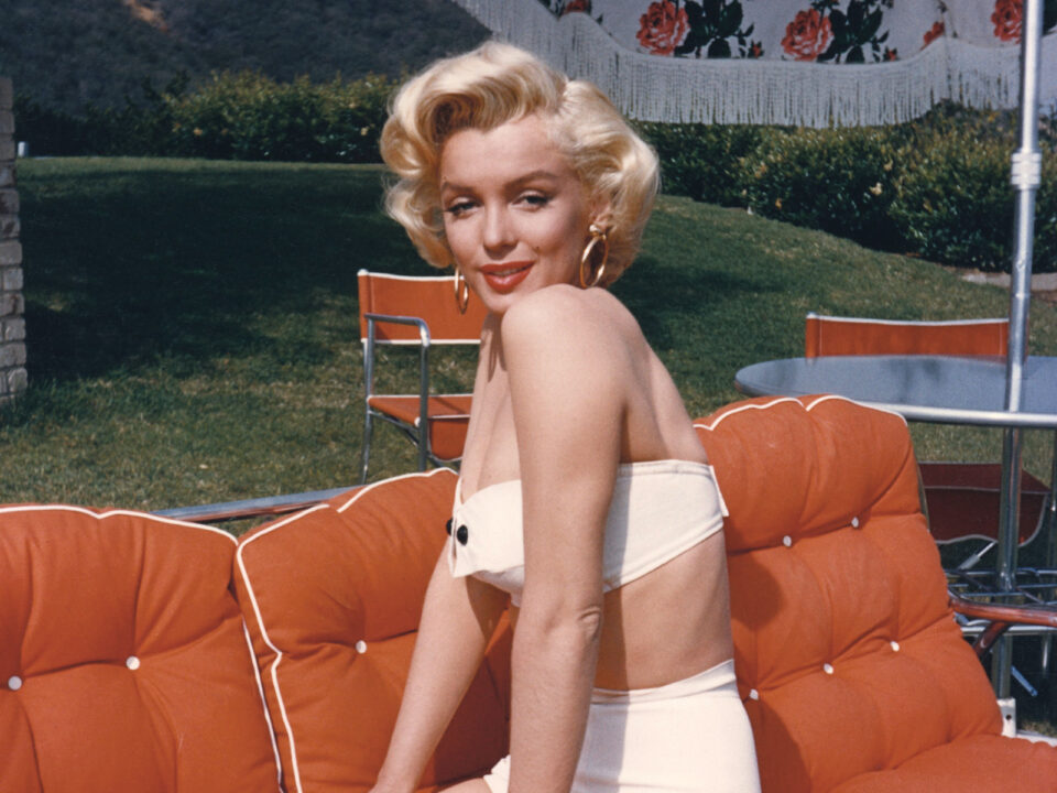 Marilyn Monroe - Nők Lapja Marilyn Monroe fehér kétrészes fürdőruhában egy narancsárgás-pirosas kerti kanapén