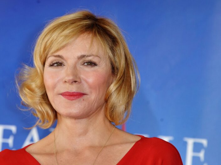 Kim Cattrall kék háttér előtt vörös ruhában fintorog