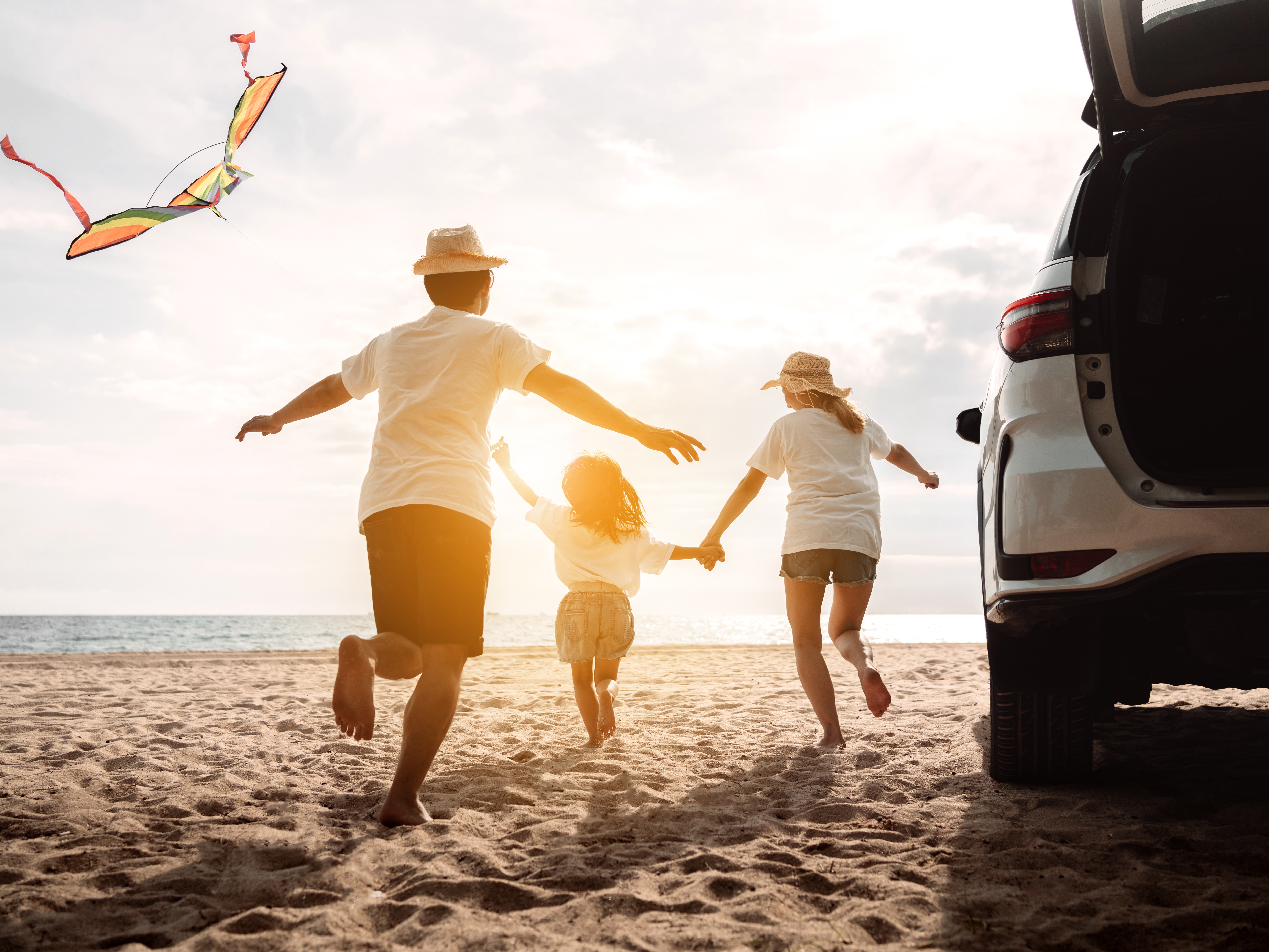 Happy Family with car travel road trip summer vacation in car in the sunset Dad mom and daughter happy traveling enjoy together driving in holidays people lifestyle ride by automobile - Nők Lapja Háromtagú család egy autó mellől a tenger felé szalad a homokos parton