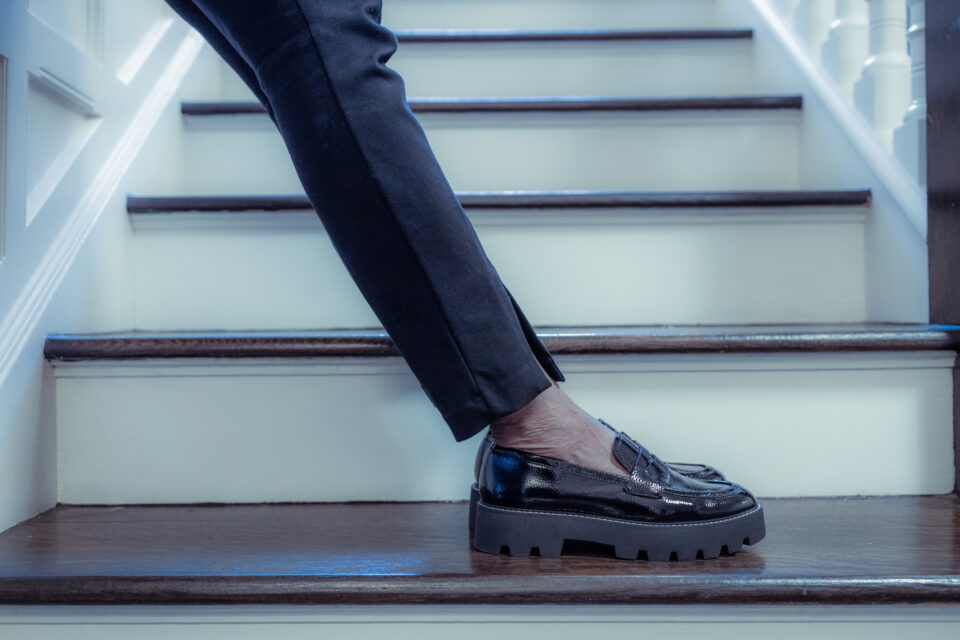 black woman standing on stairs wearing black pants black loafers - Nők Lapja 50-felett-kiegeszito-divat