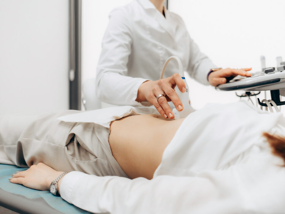Closeup of male doctor moving ultrasound probe on pregnant womans stomach in hospital - Nők Lapja