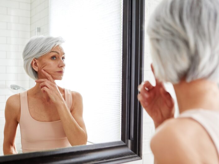 középkorú nő az arcbőrét vizsgálja
