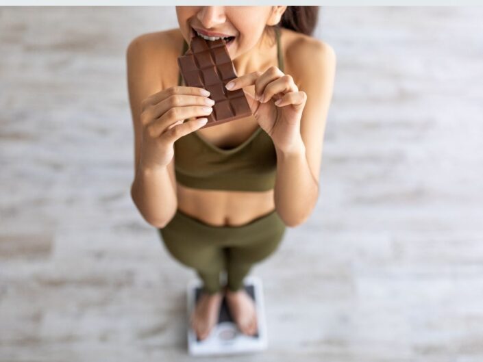 mérlegen álló nő csokit eszik