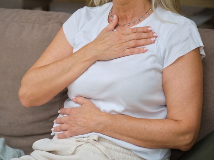 fehér póló nő kanapé kéz mellkason hason fájdalom