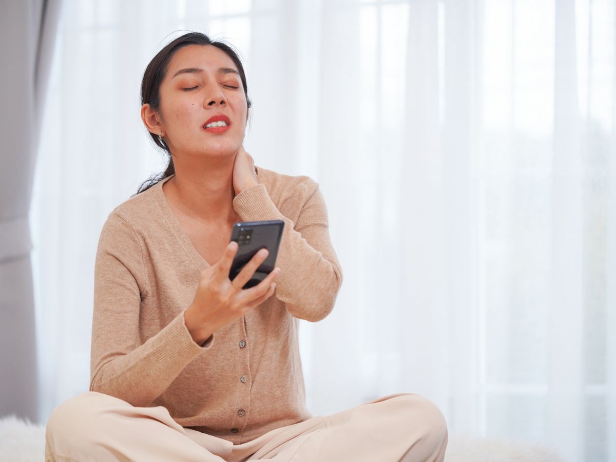 okostelefont használó nő nyakfájással küzd, sms-nyak szindróma
