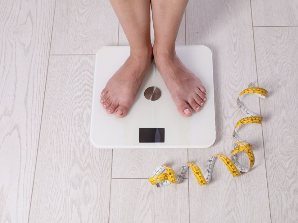 mérlegen álló nő mérőszalaggal