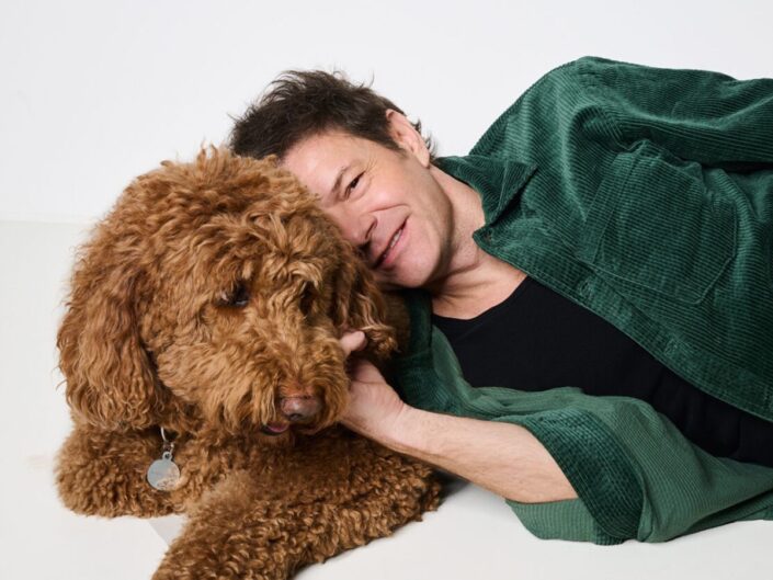 Till Attila Tilla fekszik zöld ingben, fejét a barna kutyáján pihenteti