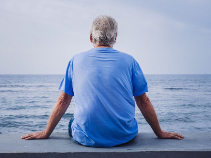idős férfi ül magányosan a vízparton