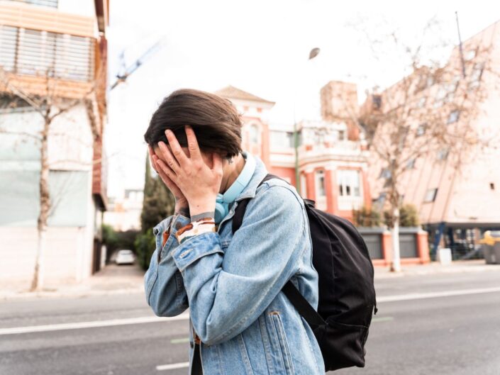 Szomorú nő sétál az utcán nappal, miközben kezével eltakarja az arcát.