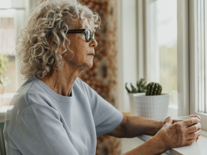 szőke középkorú szemüveges nő ablak előtt ül mereng kifelé néz