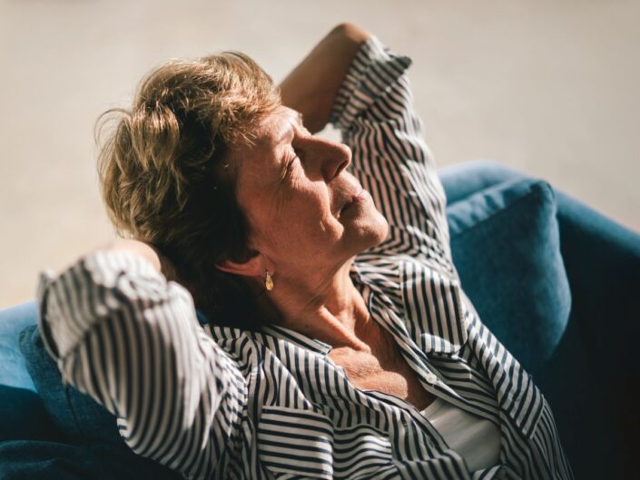 idősebb nő csukott szemmel a napnak fordulva pihen egy kanapén