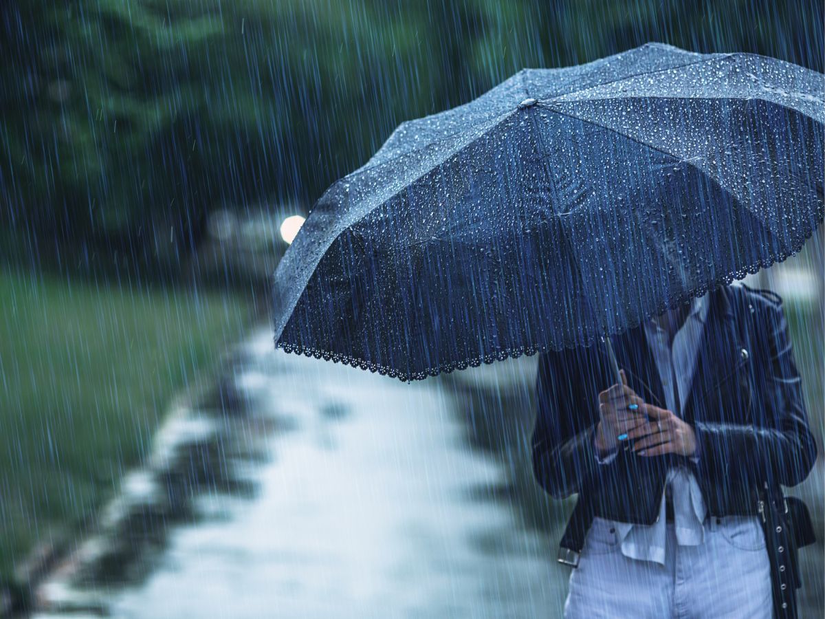 nő esőben sétál kezében egy esernyővel