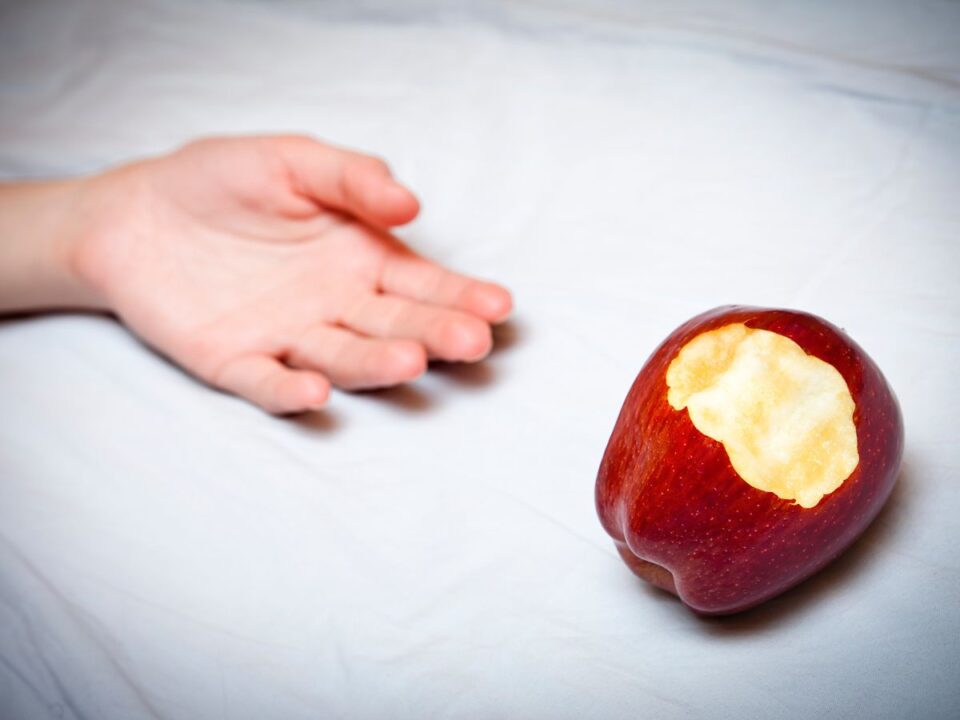 fehér lepedőre hanyatló kéz mellette egy piros alma harapásnyommal