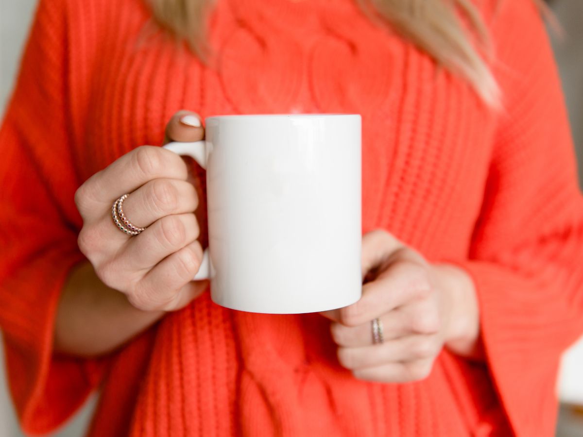 narancssárga pulóveres szőke nő fehér bögrét tart a kezében