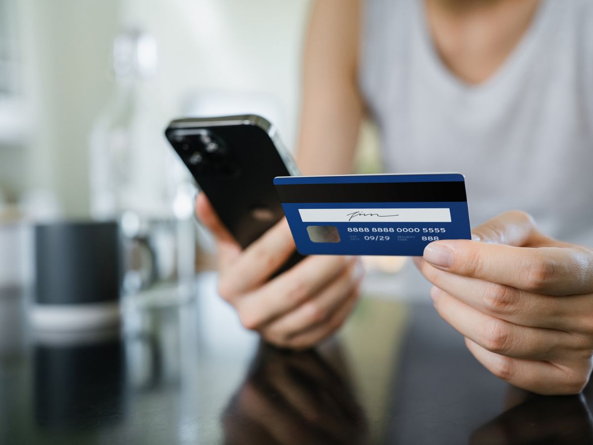 nő telefonnal és hitelkártyával a kezében