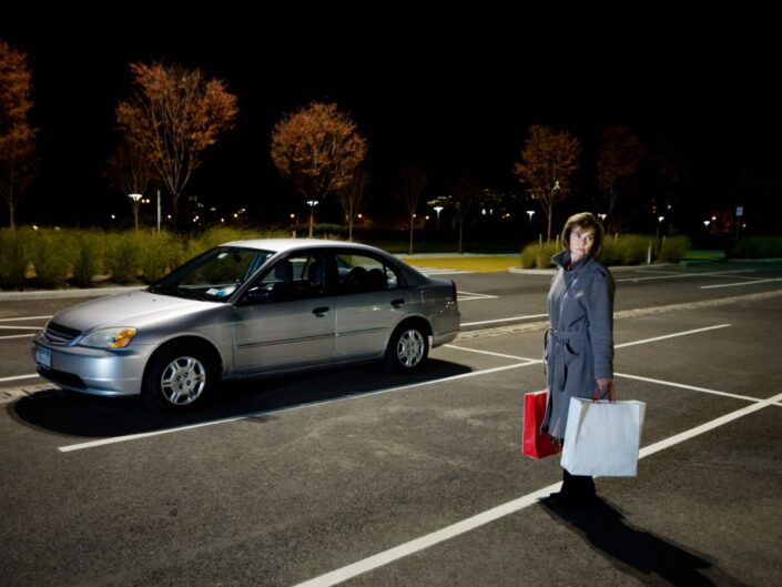 nő szatyrokkal egyedül sötétben egy parkolóban az autója mellett