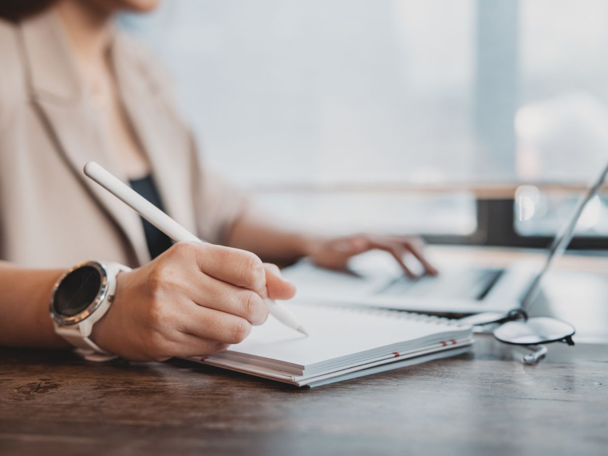 egy nő egy számítogép mellett papírra jegyzetel