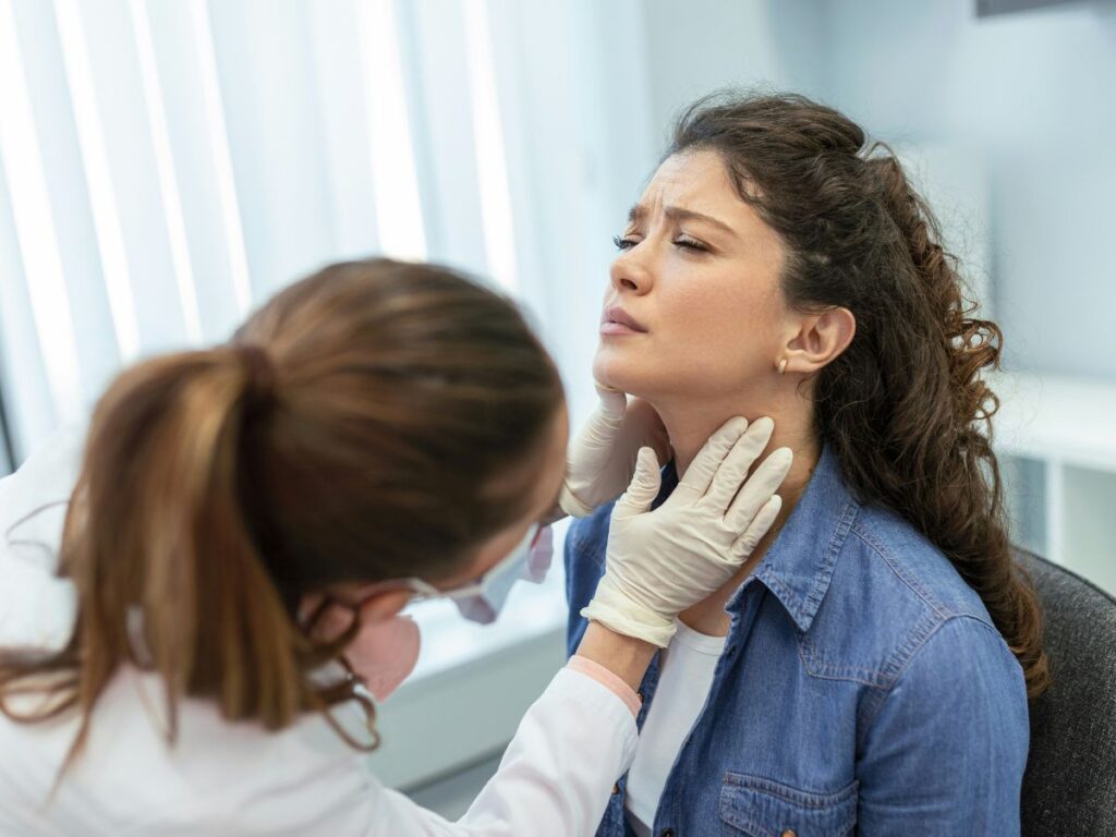 cicada-covid-varians-tunetek-torokfajas - Nők Lapja Barna, hosszú hajú nő fájó torkát vizsgálja tapintással orvos gumikesztyűben
