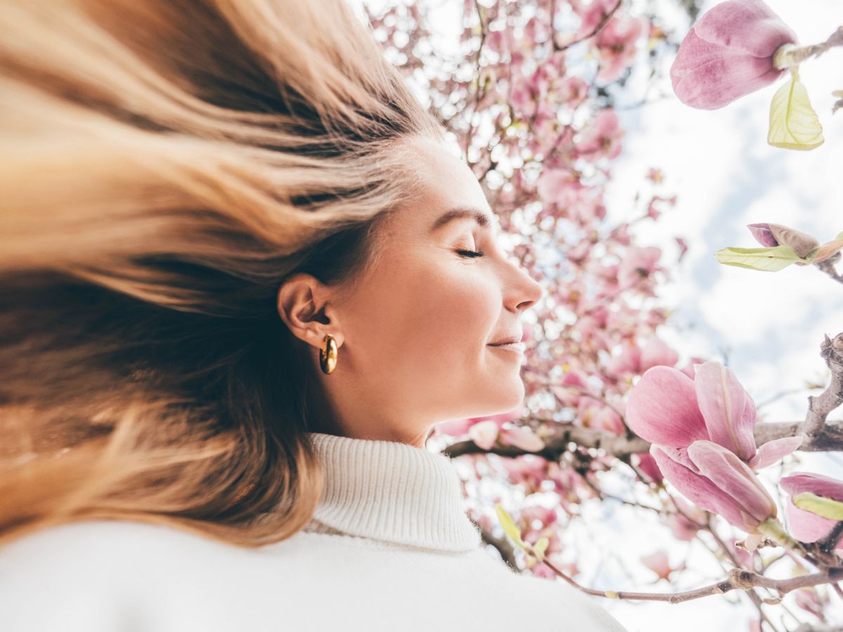 Egy derűs szőke nő profilportréja csukott szemmel, rózsaszín magnóliavirágokkal körülvéve tavasszal.