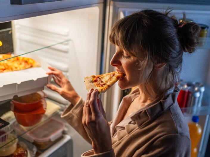 nő pizzát eszik a nyitott hűtőnél