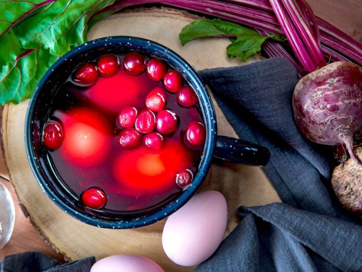 Egy sötét tálban mélyvörös céklalében tojások áznak, körülöttük cékladarabok és levelek. A természetes festőlé intenzív színt ad, a környezet rusztikus, konyhai hangulatot idéz.