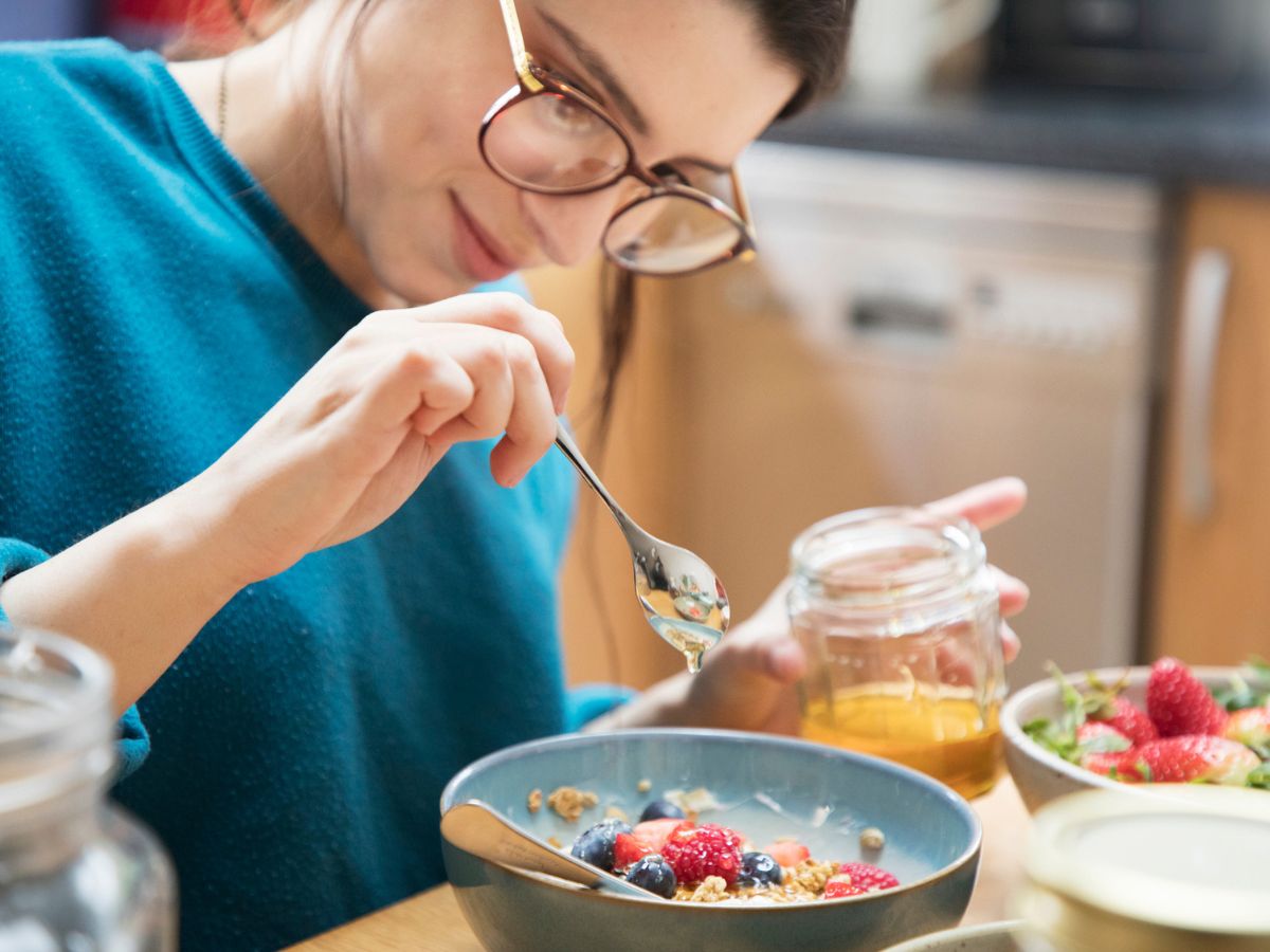 fiatal nő szemüvegben reggeli tányér méz gyümölcsök