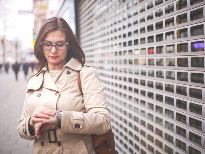 középkorú nő nézi az óráját az utcán