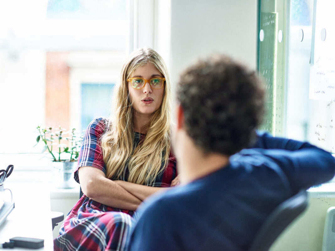 szőke nő keresztbe font kézzel ül a kanapén egy férfival, aki háttal van