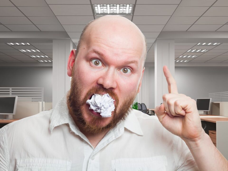 Egy szakállas férfi irodai környezetben gyűrt papírt tart a szájában, miközben felemelt ujjal magyaráz. A jelenet a nem ehető dolgok fogyasztását mutatja, ami a pica egyik szélsőséges példája.