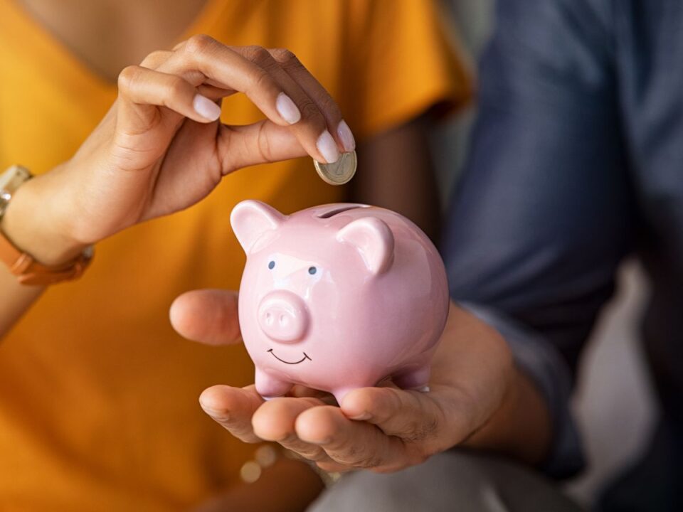 sporolas-tippek-30-napos-terv - Nők Lapja Egy kéz érmét dob egy rózsaszín malacperselybe, miközben a másik kéz tartja azt. A jelenet a tudatos spórolást és az apró megtakarítások erejét szimbolizálja.