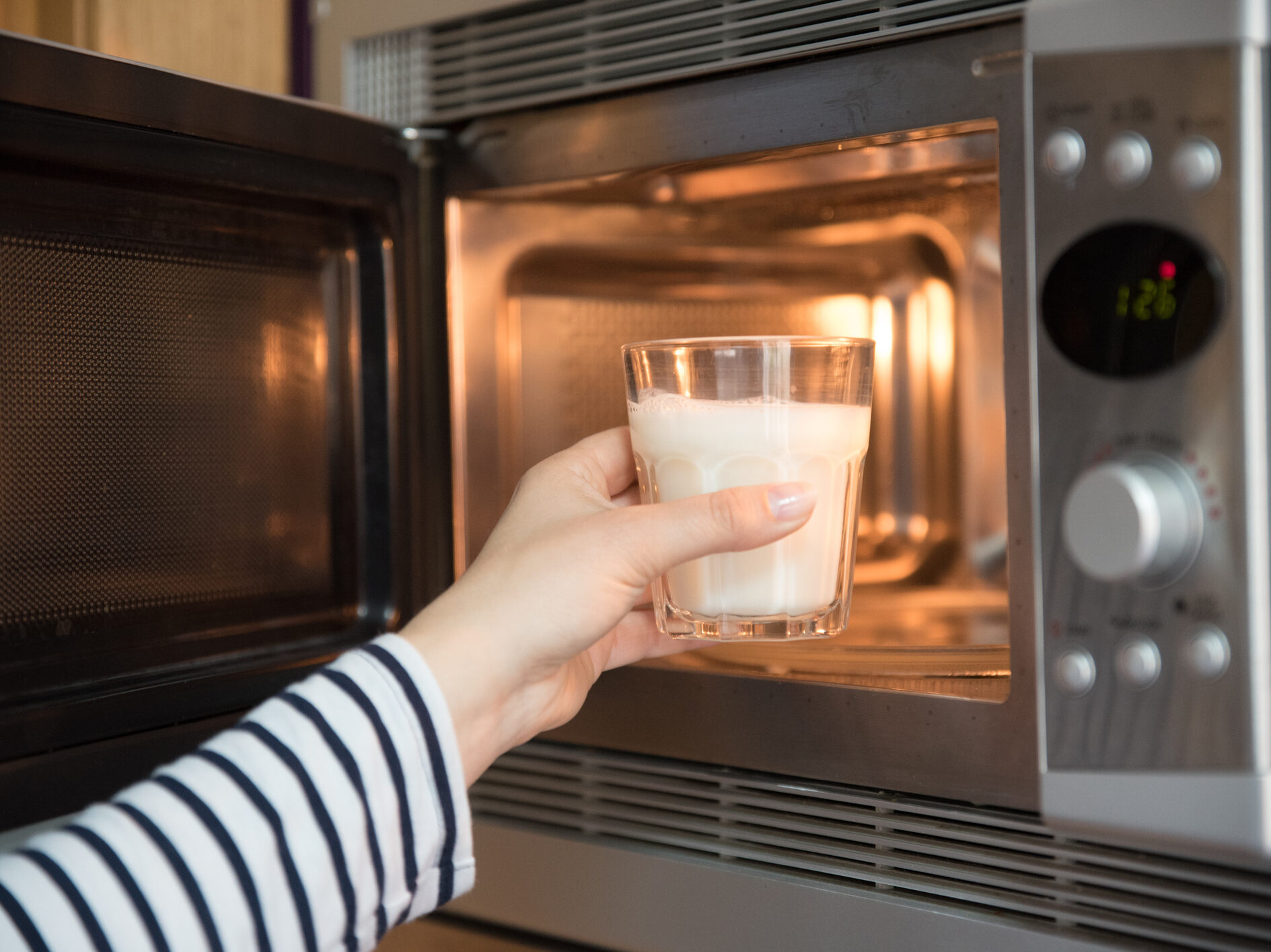 női kéz behelyez egy tejes poharat a mikróba