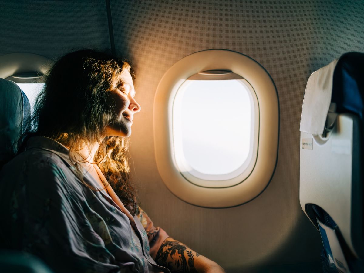repülőn utazó nő élvezi az ablakon bejövő napfényt