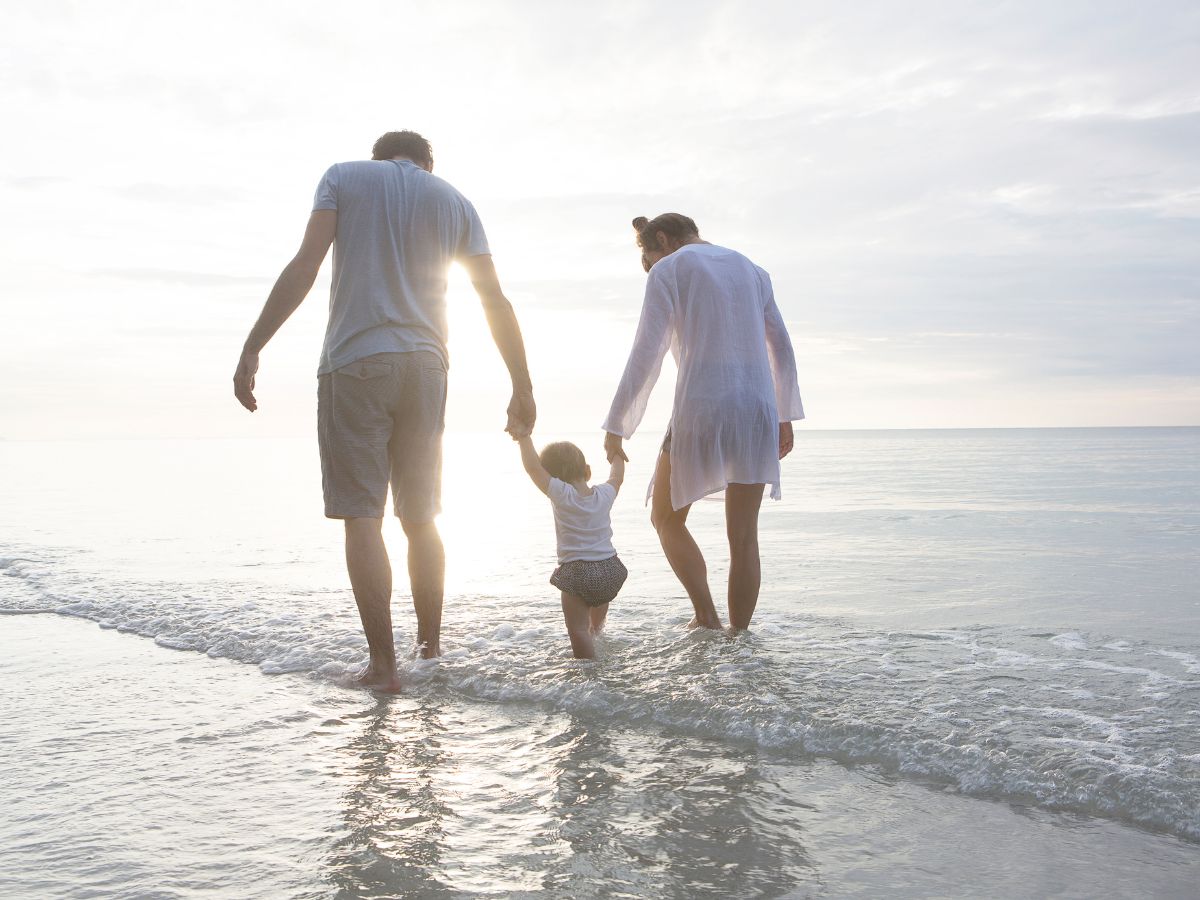 tengerparton sétálnak szülők kisgyerekkel