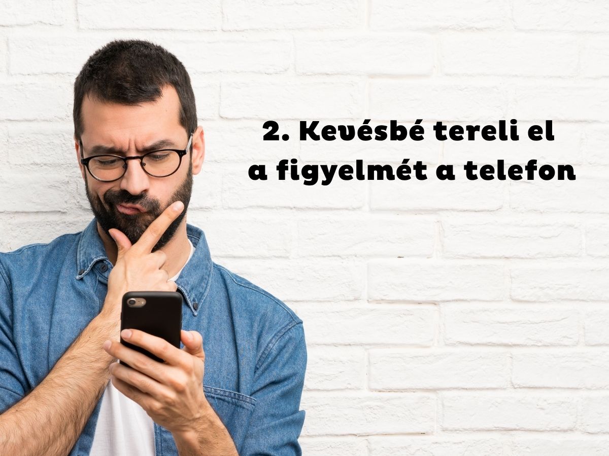 Szemüveges és szakállas férfi farmeringben állát vakarva nézi a telefonját