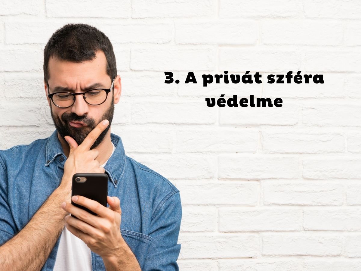 Szemüveges és szakállas férfi farmeringben állát vakarva nézi a telefonját