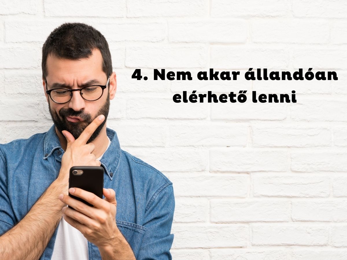 Szemüveges és szakállas férfi farmeringben állát vakarva nézi a telefonját
