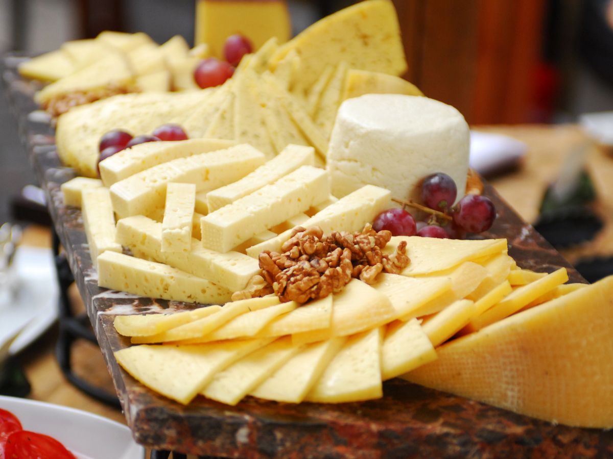 Különböző sajtfélék hosszú tálcán, olajos magvakkal, gyümölccsel