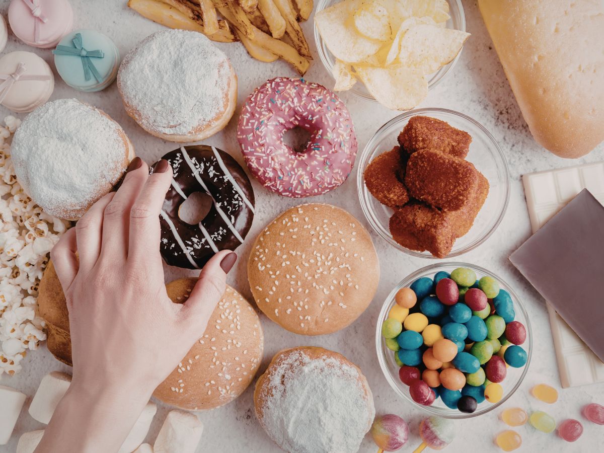 Női kéz nyúl csokimázas fánkért, különböző nassolnivalók az asztalon