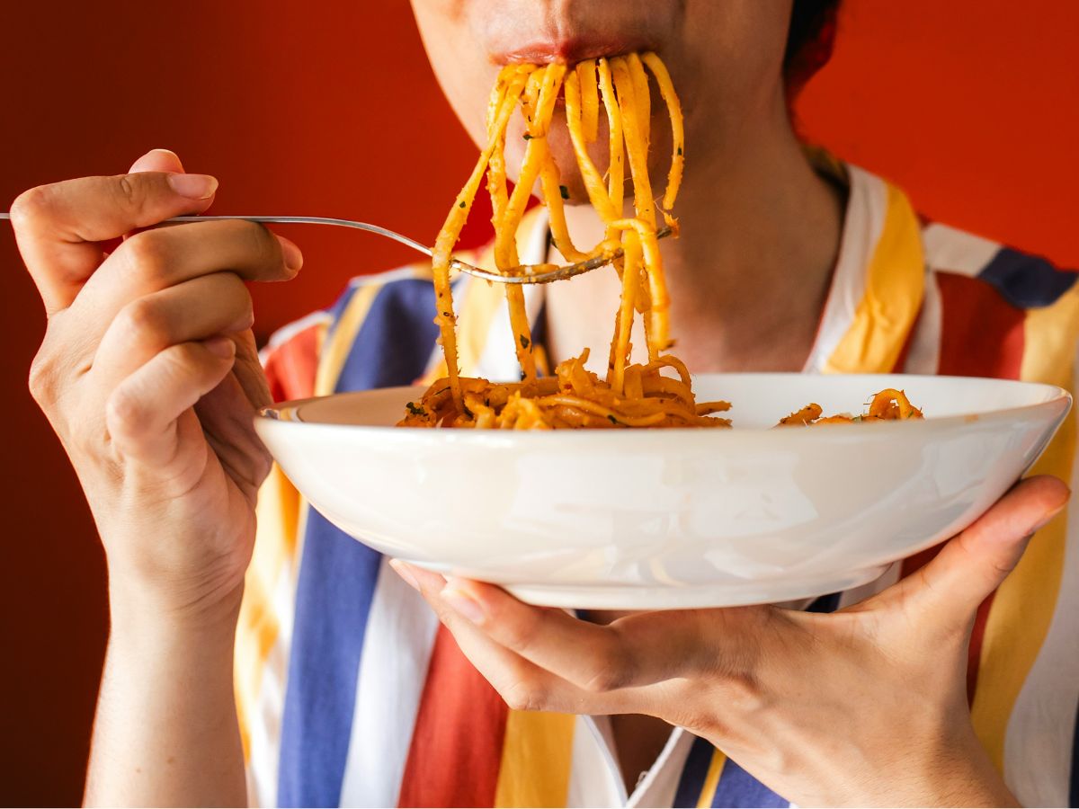 Nő fehér tányérból csíkos ingben paradicsomos spagettit eszik