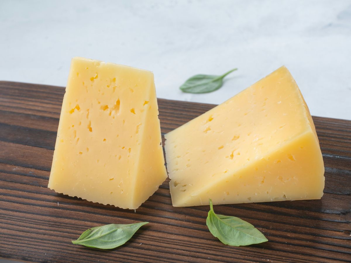 Gouda sajt két háromszögnyi szelet fa tálcán, falevelek körülötte