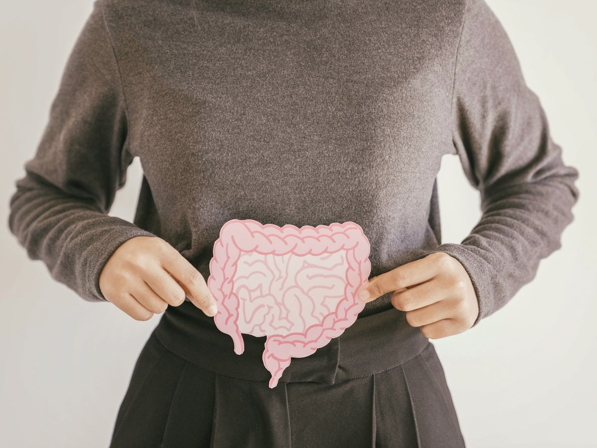 Nő szürke felsőben és nadrágban a bélrendszert ábrázoló rajzot tart a hasa elé