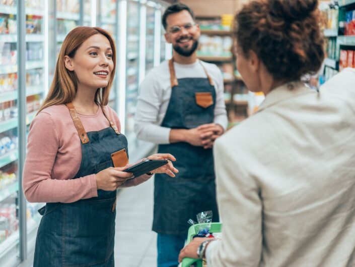 Bolti eladók beszélnek háttal álló női vásárlóhoz