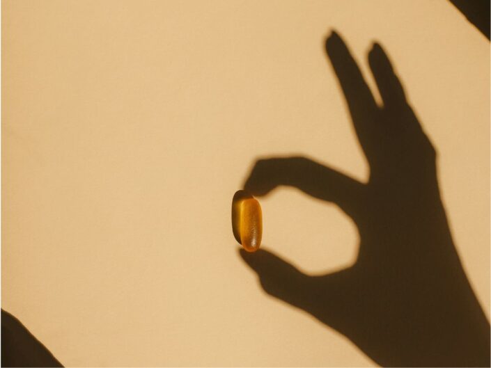 Kéz árnyéka, mintha D-vitamin kapszulát tartana a mutató- és hüvelykujja között