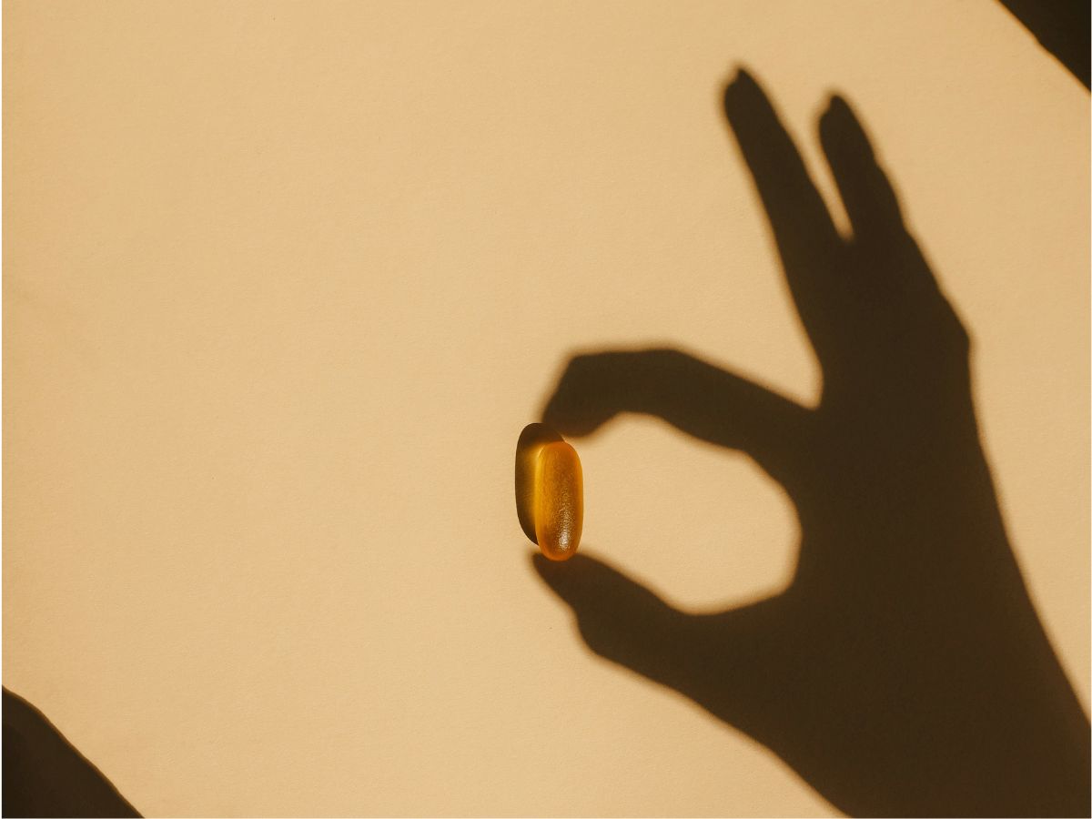 Kéz árnyéka, mintha D-vitamin kapszulát tartana a mutató- és hüvelykujja között