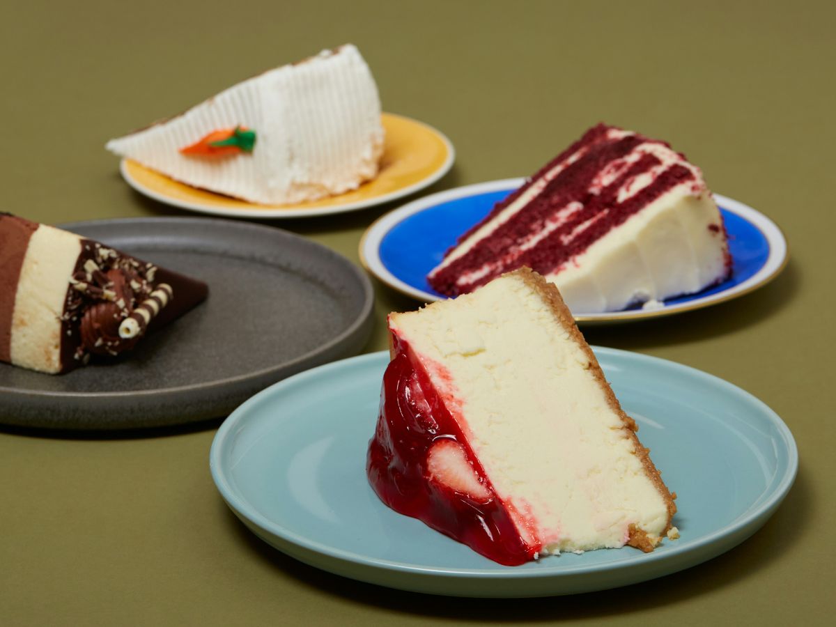 Négy különböző tányéron négy különböző sütemény, csokis, gyümölcsös, sajttorta, répatorta, okkerszínű háttér