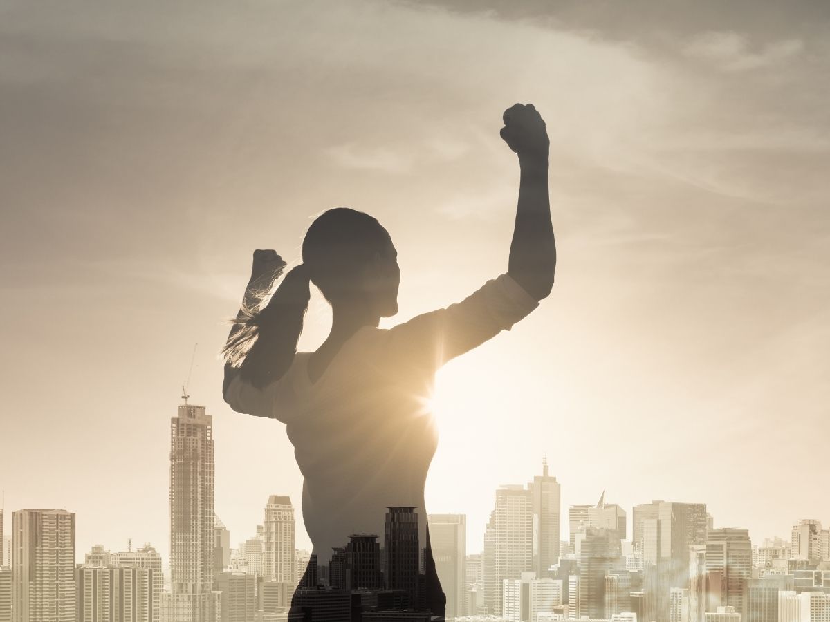 erős nő feltartott karokkal egy város sziluettje előtt