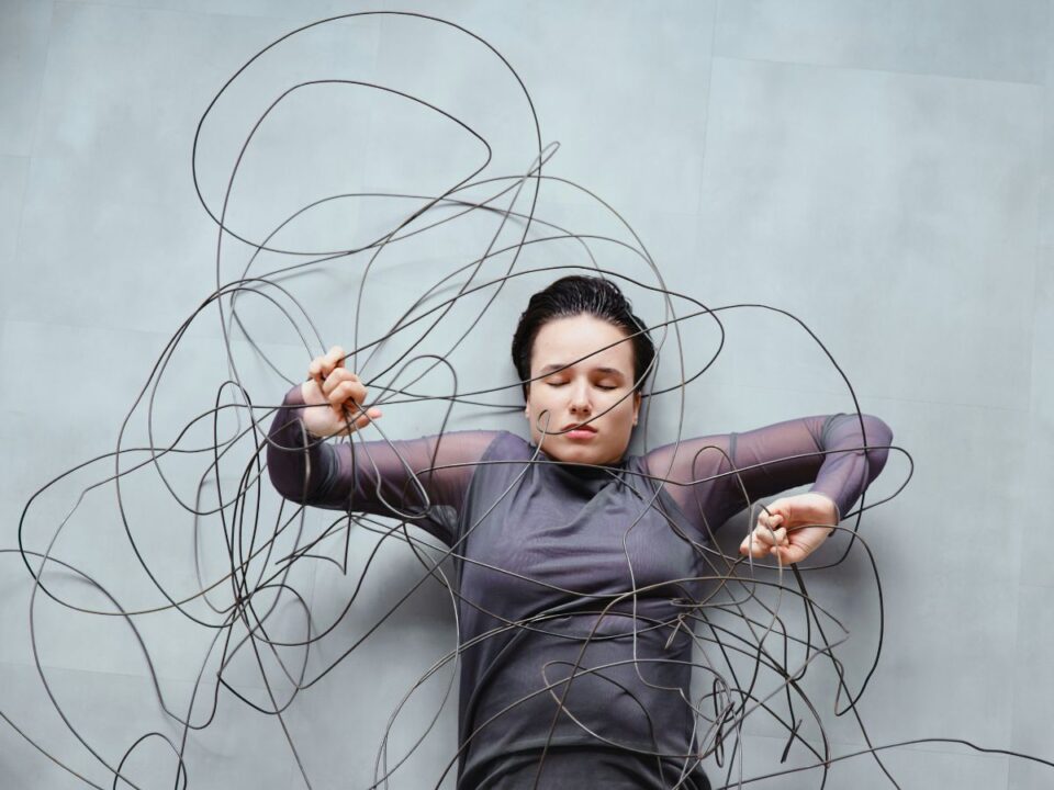 Nő szürke felsőben szürke padlón fekve zsinórkompozícióba keveredve