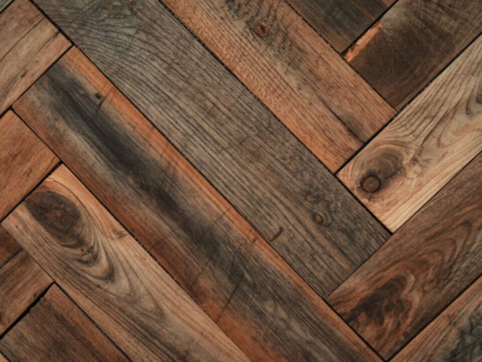 Halszálka mintában lerakott, barna árnyalatú fa parketta közelről, természetes erezettel és enyhe kopásnyomokkal, meleg tónusú felülettel.