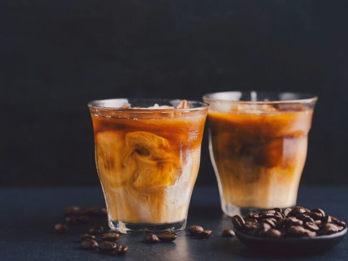 Két pohár ananászlével édesített jeges kávé üvegpohárban, fekete háttér, körülöttük kávébabok